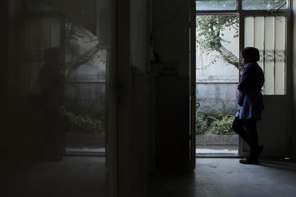 Sunless Shadows. Une jeune détenue en Iran observe l'extérieur dès la porte de la prison.